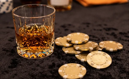 Kristallglas mit bernsteinfarbenem Getr&auml;nk neben goldenen Casino-Chips auf dunklem Samt